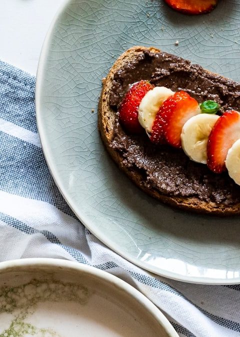 Top view of a healthy breakfast setup featuring toast with nut spreads, fresh fruits, and natural light on a minimal table setting.