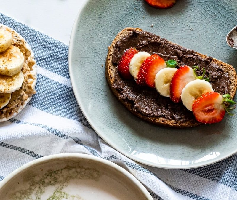 Top view of a healthy breakfast setup featuring toast with nut spreads, fresh fruits, and natural light on a minimal table setting.