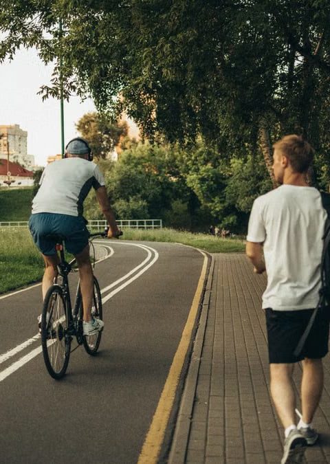 A cyclist and a walker enjoy a peaceful park trail surrounded by greenery.