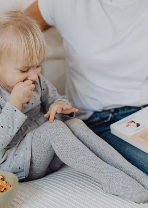 A mother and daughter enjoying storytime on a cozy couch with snacks nearby.