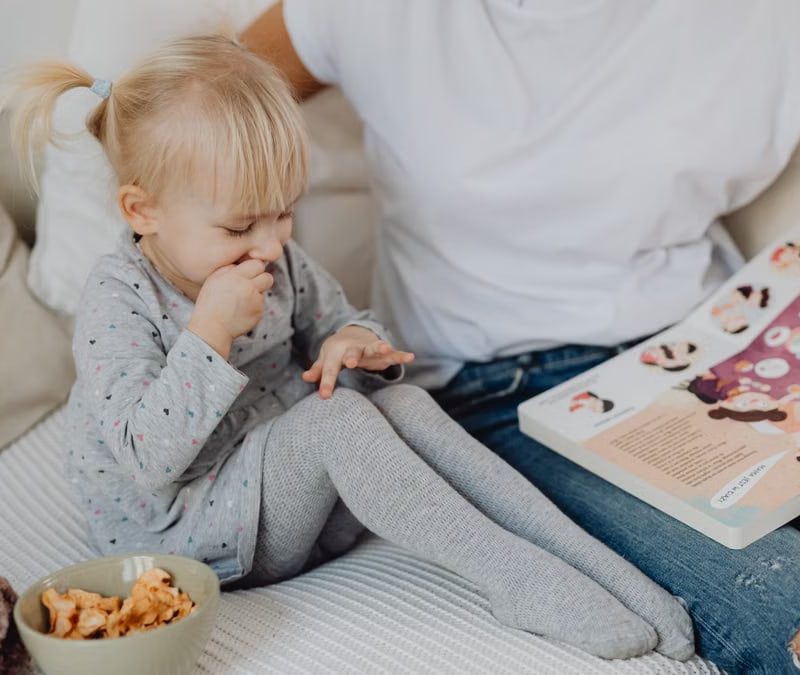 A mother and daughter enjoying storytime on a cozy couch with snacks nearby.